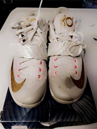 a pair of white and gold nike basketball shoes on top of a box